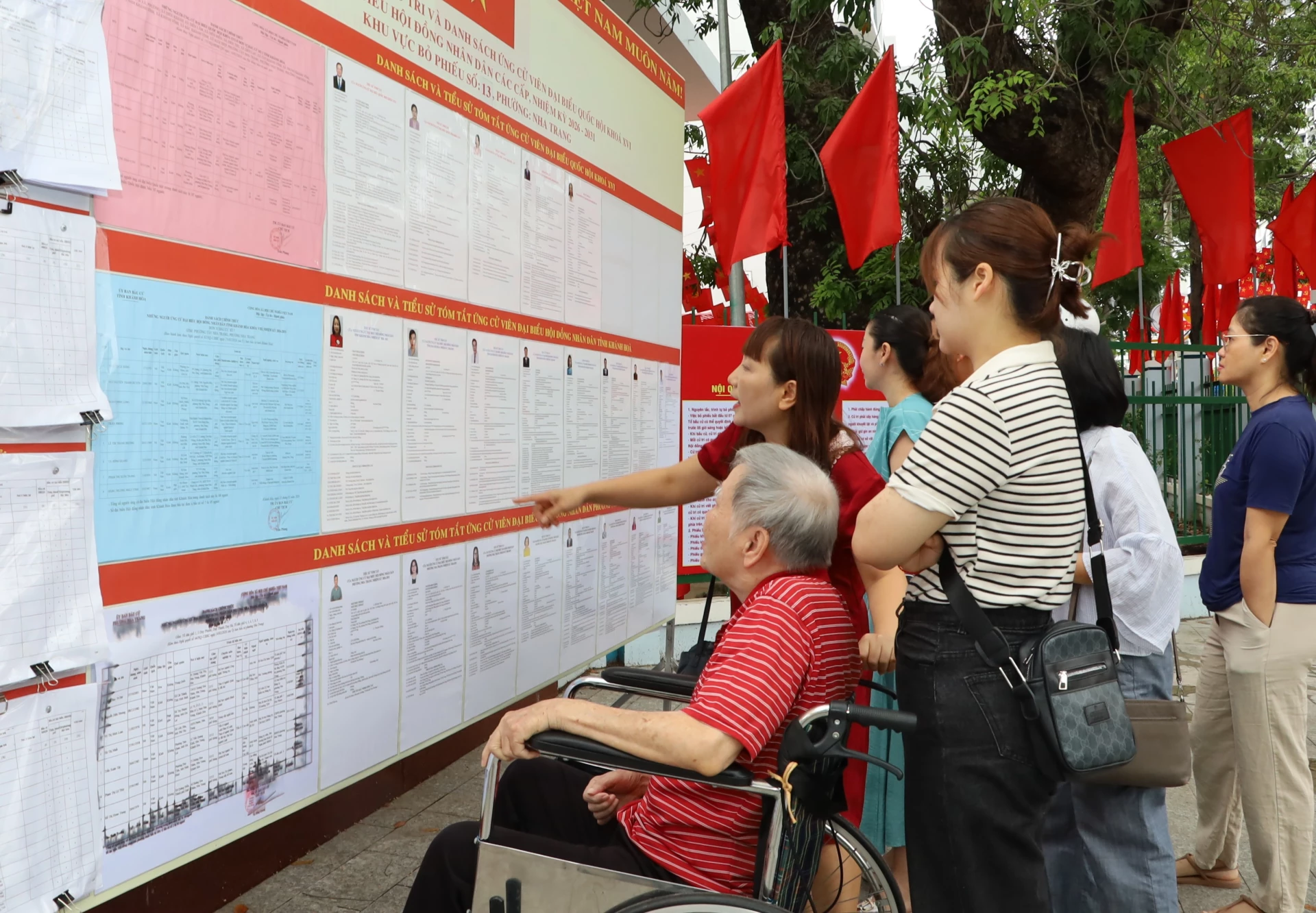 Dù phải ngồi xe lăn, nhưng ông Ngô Toàn, 88 tuổi phường Nha Trang vẫn cùng con, cháu để khu vực bỏ phiếu tìm hiểu thông tin người ứng cử trước khi vào khu vực bỏ phiếu lựa chọn những đại biểu xứng đáng. Ảnh: Văn Giang.