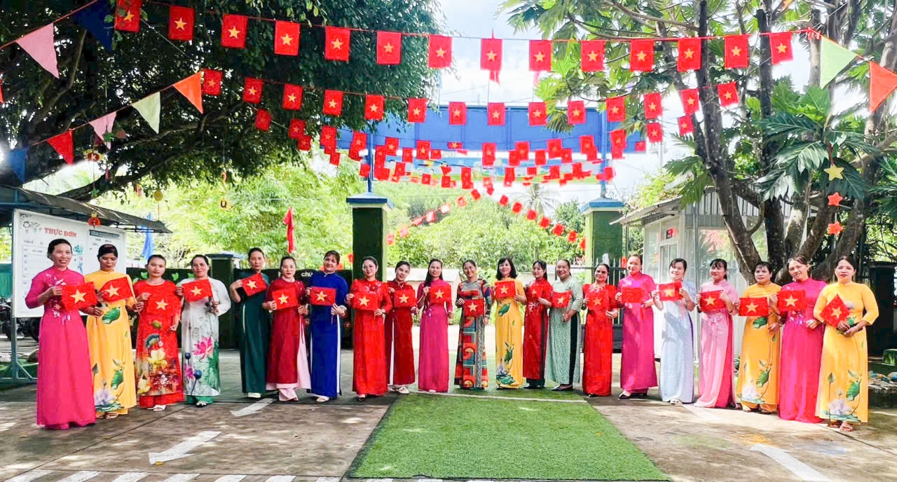 Các giáo viên Trường Mầm non Hoa Lan, xã Nam Khánh Vĩnh chụp hình trong trang phục áo dài bên lá cờ Tổ quốc.