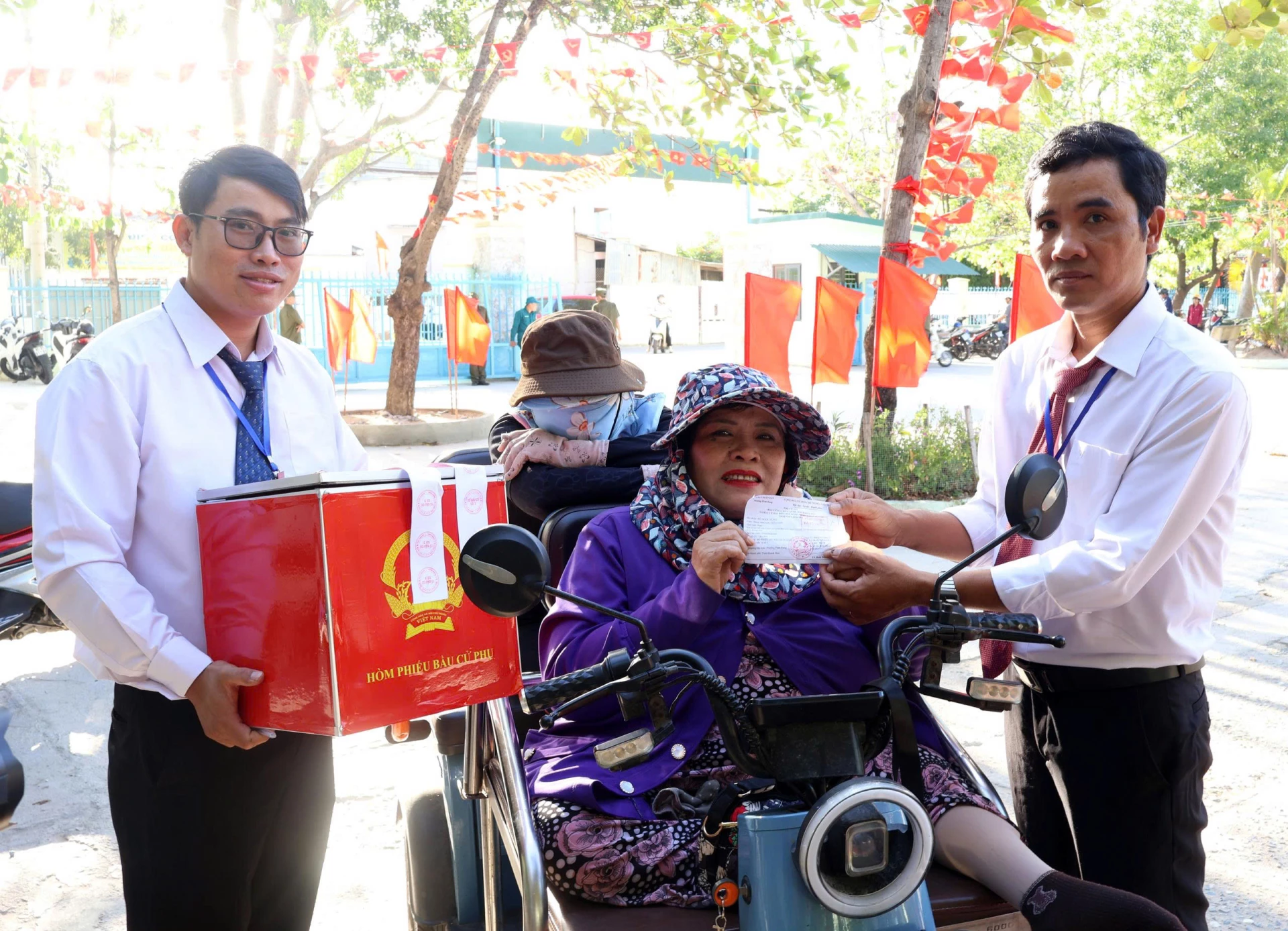 Thành viên Tổ bầu cử số 3, phường Phan Rang trao thẻ cử tri đã đóng dấu hoàn thành việc bỏ phiếu cho tri là người khuyết tật. Ảnh: Lâm Anh.