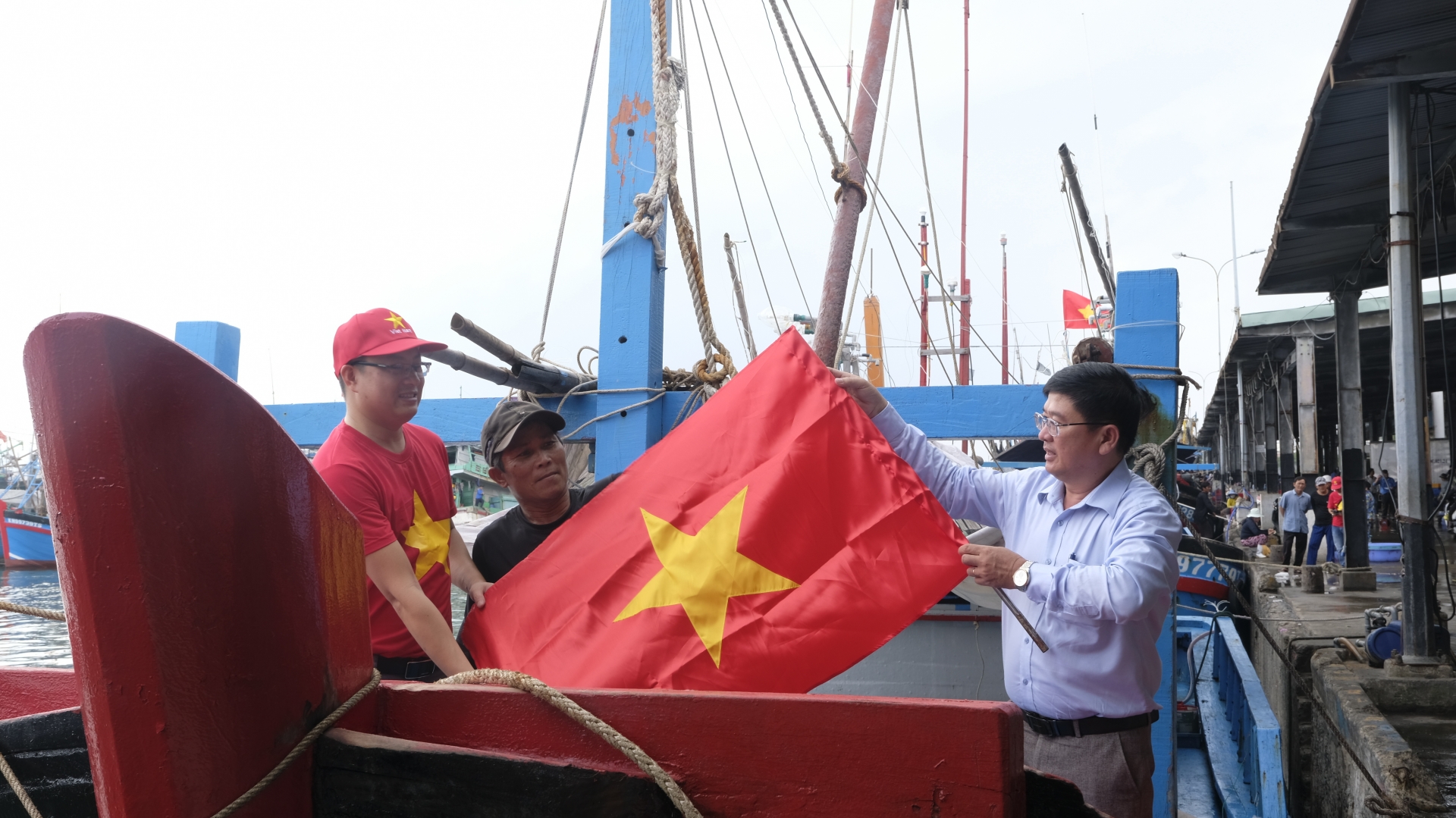 Ông Lê Hoàng Triều - Phó Tổng Biên tập Báo Khánh Hòa (bên phải) cùng lãnh đạo Công ty Cổ phần Tập đoàn DVA Holdings cùng ngư dân thay mới cờ Tổ quốc trên tàu cá.