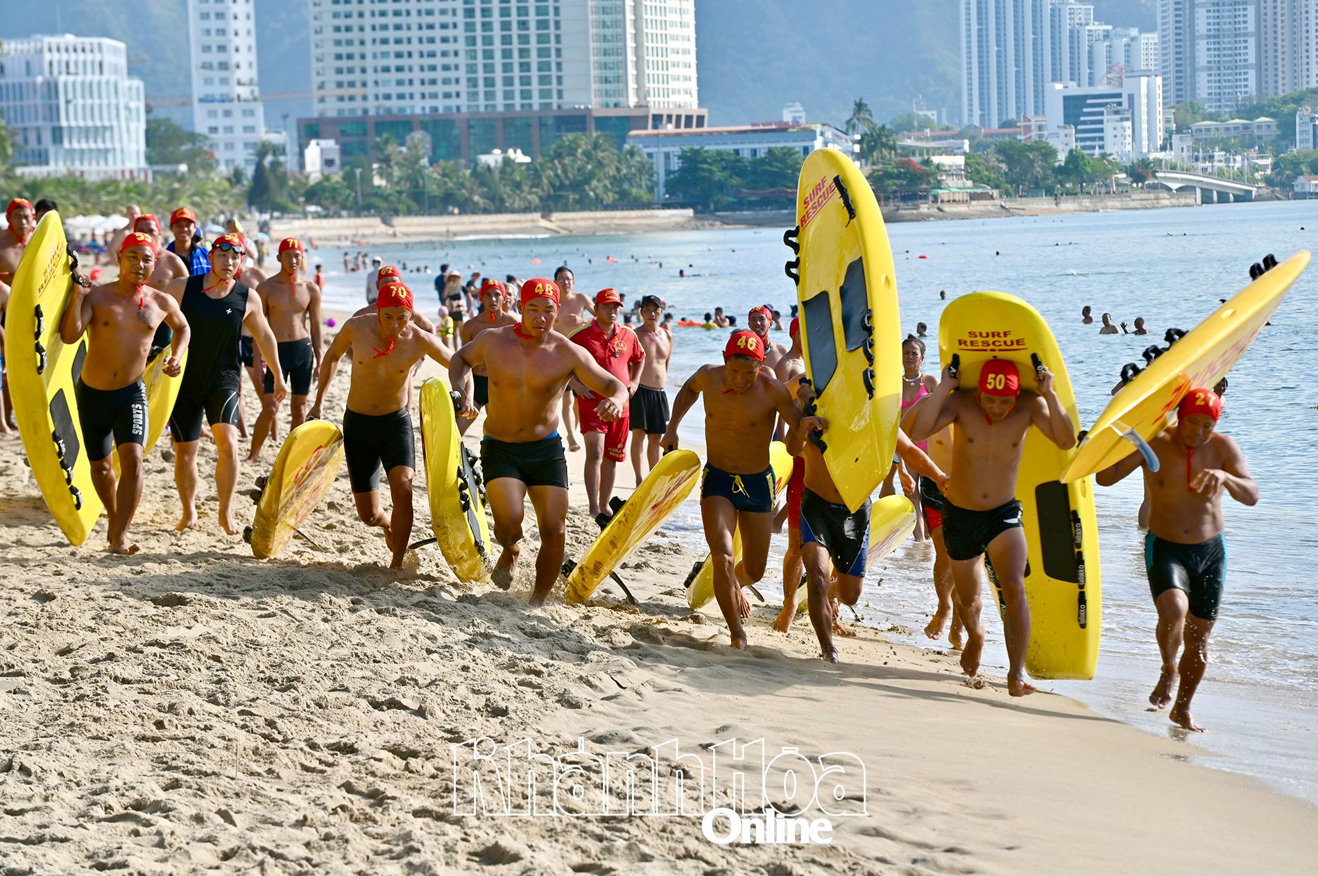 Các vận động viên mang theo ván lướt chạy trong phần thi bơi ván tiếp sức.