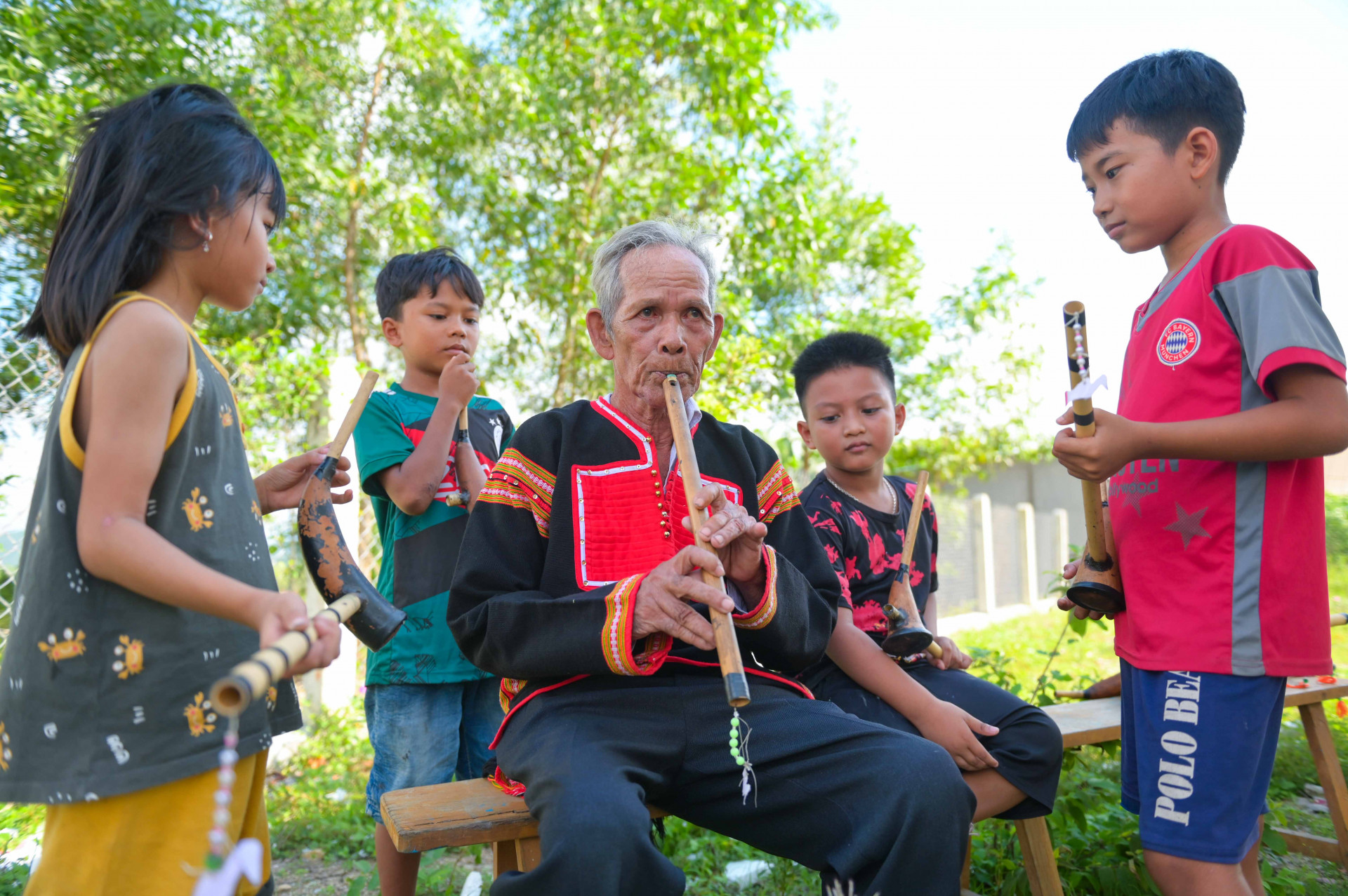 Già làng Y P’Ranh đang thổi một khúc bằng sáo trúc cho các cháu nhỏ nghe. 