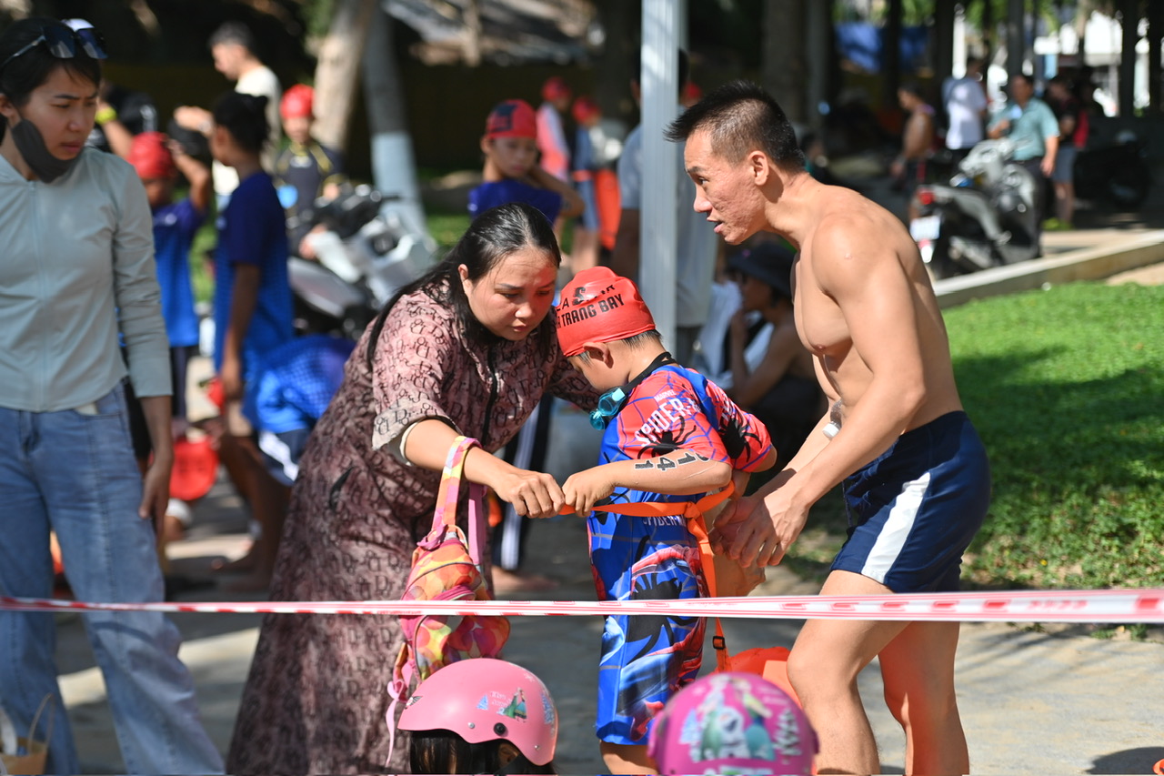 A litter swimmer is helped by his parents with life preserver

