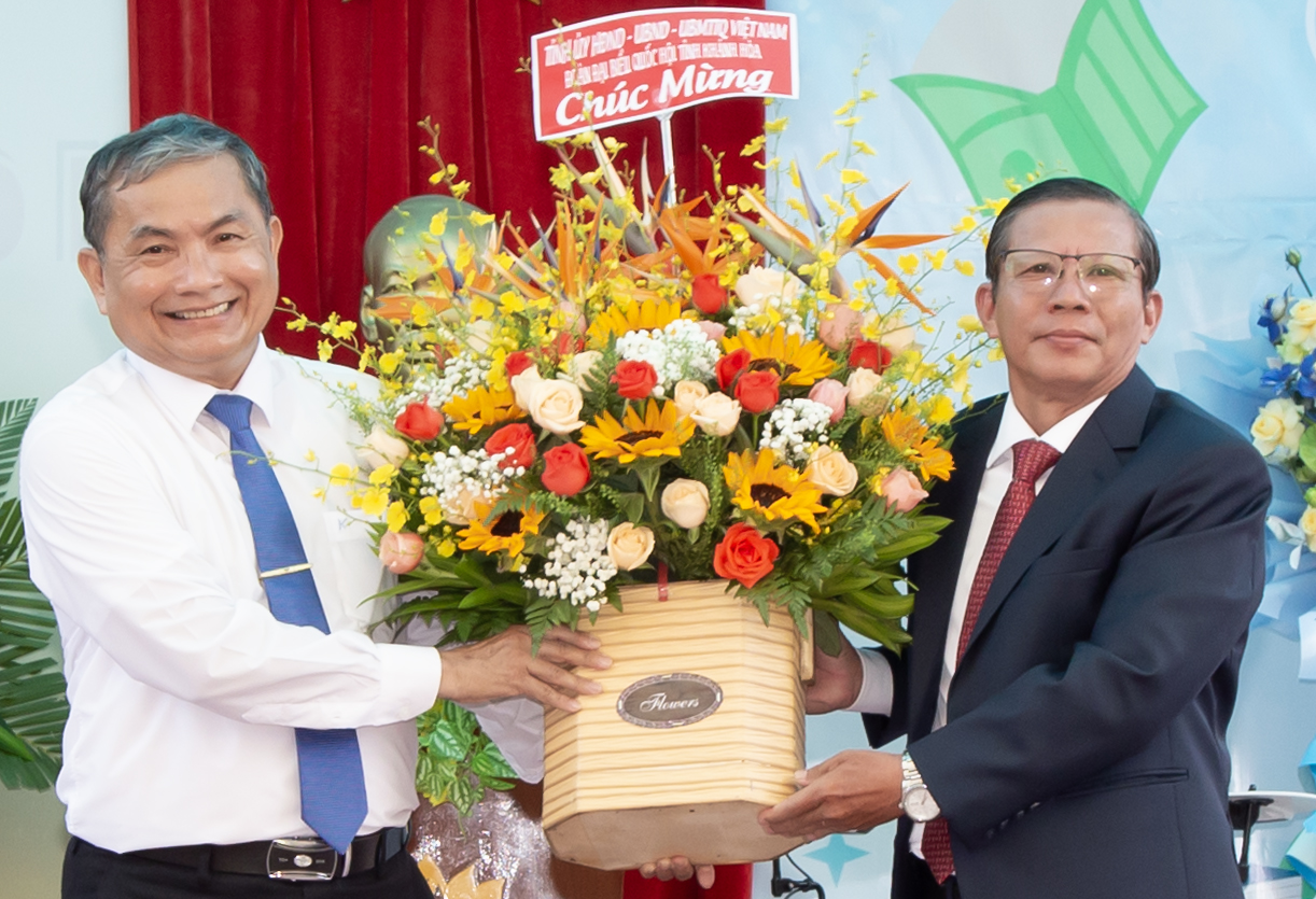 Ông Trần Ngọc Thanh (bên phải) trao hoa chúc mừng nhà trường