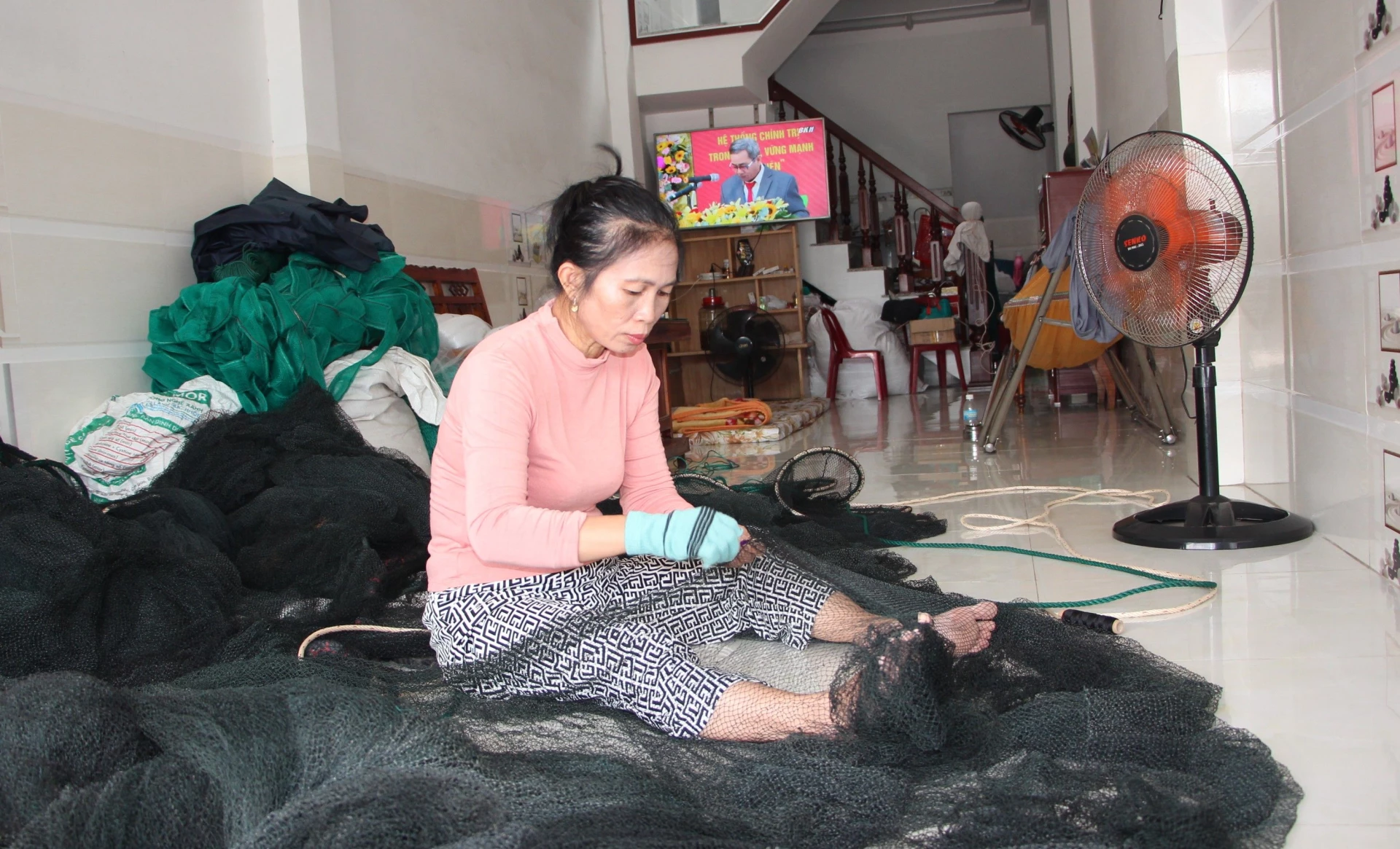 Bà Trần Thị Oanh (phường Nam Nha Trang) vừa đan vá lưới vừa theo dõi Đại hội đại biểu Đảng bộ tỉnh qua truyền hình trực tiếp của Báo và Phát thanh, Truyền hình Khánh Hòa.