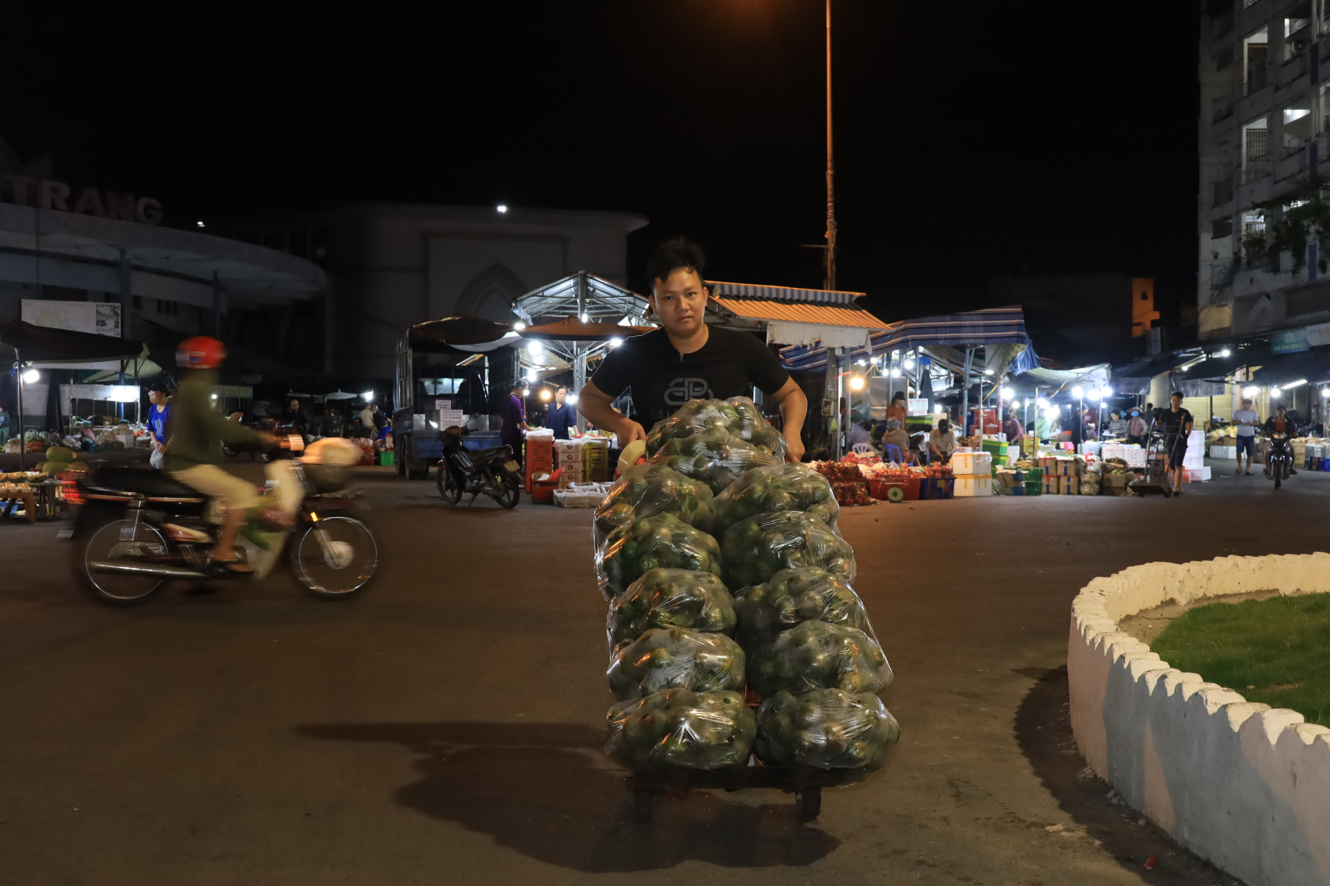 Một thanh niên vận chuyển hàng ở chợ đêm bằng phương tiện thô sơ.