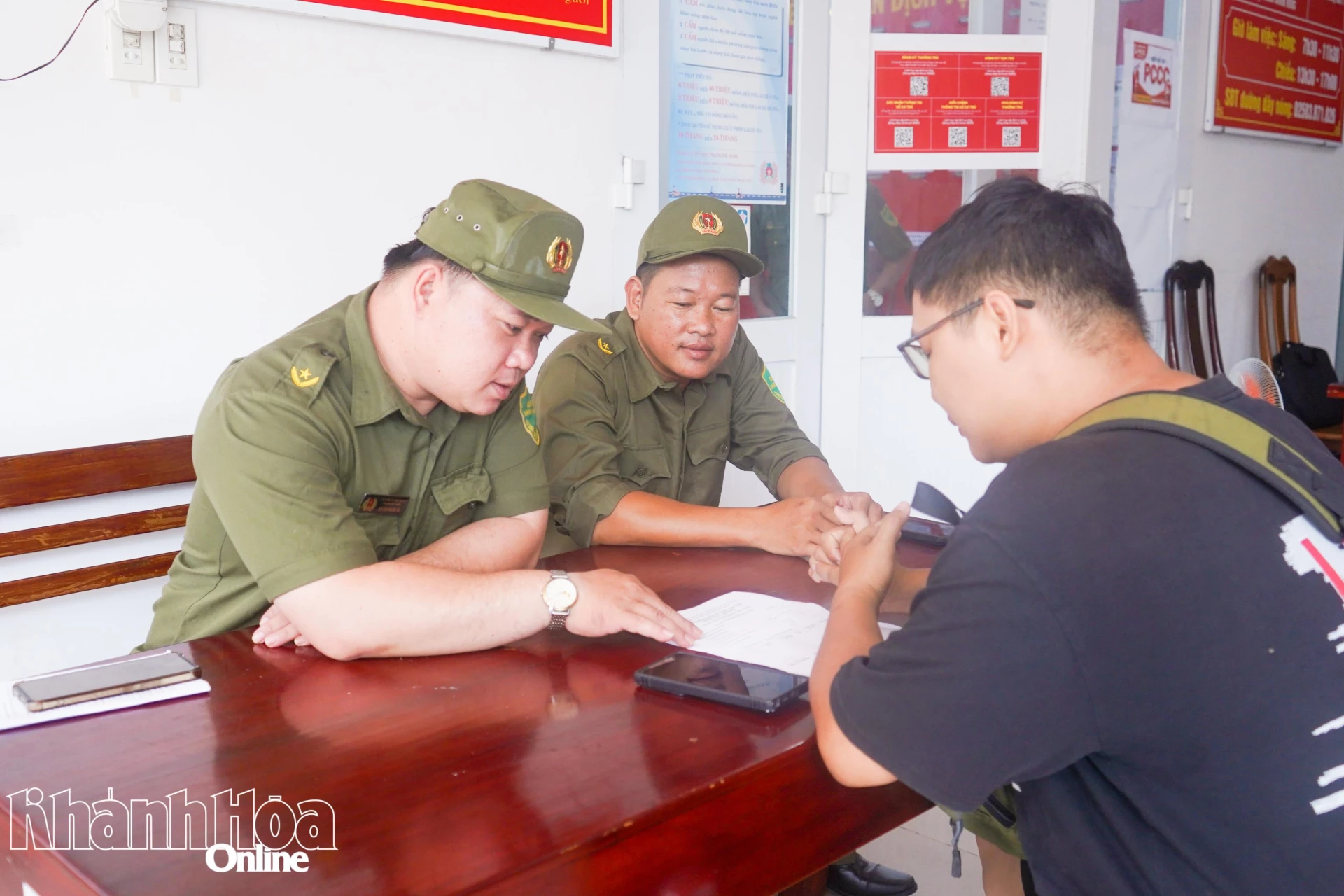 Anh Đỗ Văn Thành Tài (bìa trái) hỗ trợ người dân thực hiện 
dịch vụ hành chính công trực tuyến tại trụ sở Công an phường Nha Trang.