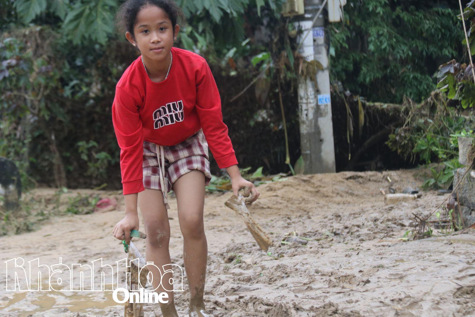 Một bé gái nhặt nhạnh những đồ đạc tại con đường ngập tràn bùn đất trong thôn