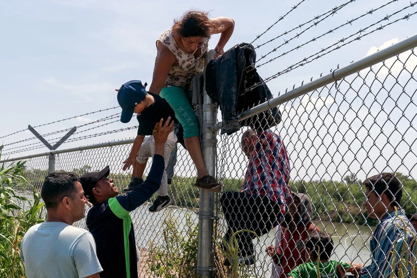 Người di cư từ Mexico trèo qua hàng rào biên giới tại Eagle Pass, bang Texas để vào Mỹ. (Ảnh: AFP/TTXVN)
