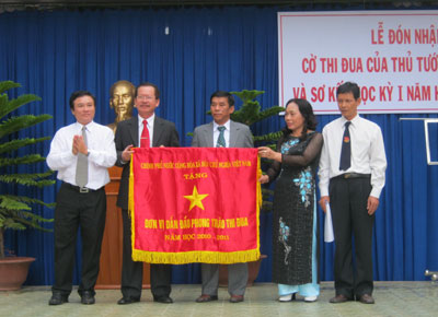 Ông Mai Thu (bìa trái) - Phó Giám đốc Sở Nội vụ, Thường trực Hội đồng Thi đua tỉnh trao Cờ thi đua của Thủ tướng Chính phủ cho lãnh đạo nhà trường.