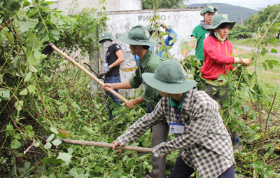 Các đoàn viên, thanh niên đang phát quang xung quanh bảng tuyên truyền.