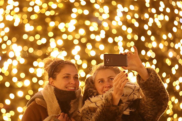 Hai du khách trẻ đến từ Mozambique (trái) và Ireland chụp selfie trước một cây thông Noel lớn tại chợ Giáng sinh thường niên ở Berlin, Đức, hôm 29/11.