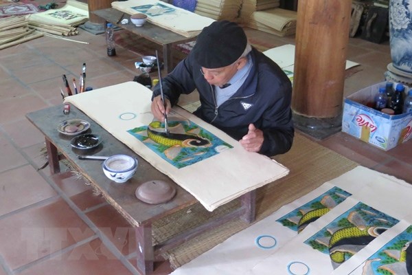Nghệ nhân Nguyễn Đăng Chế hoàn thiện bức tranh  "Cá chép trông trăng. " (Ảnh: TTXVN)
