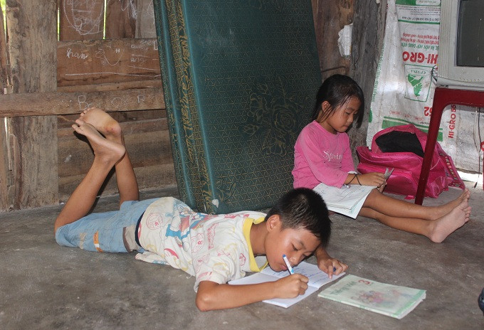 Vì gia đình quá nghèo, nên 2 con của anh Trương Ngọc Chung không có bàn học tập mà phải nằm, ngồi giữa căn nhà tạm để học bài.