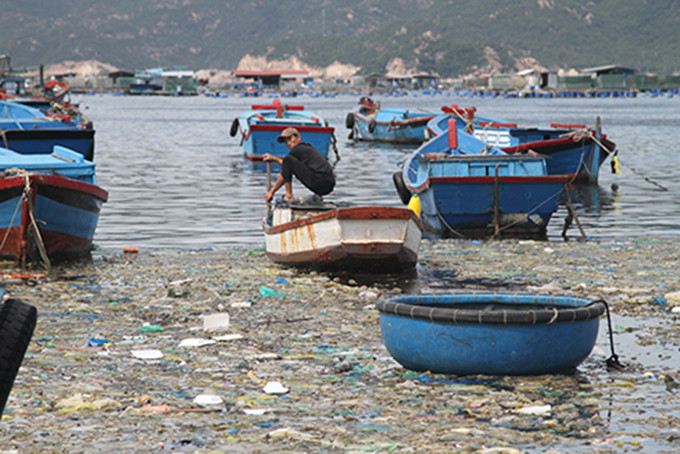 Một ngư dân đang loay hoay chèo thuyền thoát khỏi vùng biển ngập ngụa rác