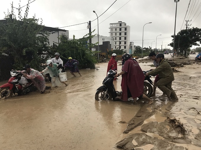 Người dân và lực lượng chính quyền xã Phước Đồng giúp đưa xe máy thoát ra khỏi bùn, đất.