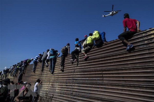 Người di cư vượt qua hàng rào biên giới giữa Mỹ và Mexico, gần cửa khẩu El Chaparral ở Tijuana, bang Baja California, Mexico. (Nguồn: AFP/TTXVN)