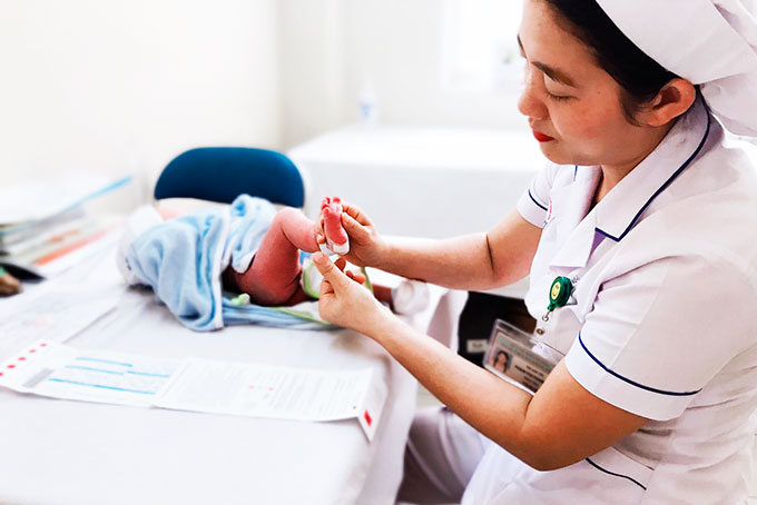 Cán bộ y tế lấy mẫu máu gót chân trẻ sơ sinh để sàng lọc sơ sinh.