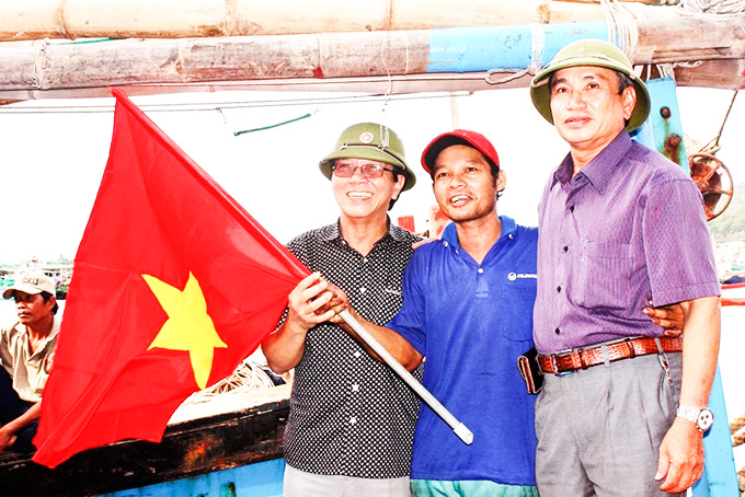 Leader of Khanh Hoa Province Labor Federation giving national flag a fishing boat owner