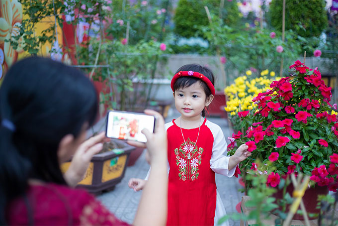 Một bé gái xúng xính váy áo đang tạo dáng chụp ảnh tại không gian chợ hoa rực rỡ ở Vincom.