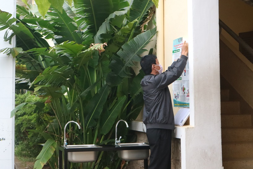 Thầy Trương Minh Trình, Phó Hiệu trưởng phụ trách Trường THPT Lý Tự Trọng dán tờ rơi tuyên truyền các biện pháp phòng chống dịch. Bên cạnh là 2 trong số 10 bồn rửa tay mới được lắp đặt tại trường. 