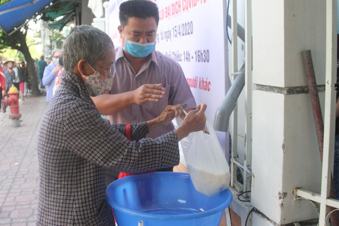 Thành viên của Ban tổ chức chương trình ATM gạo hỗ trợ một người già nhận gạo