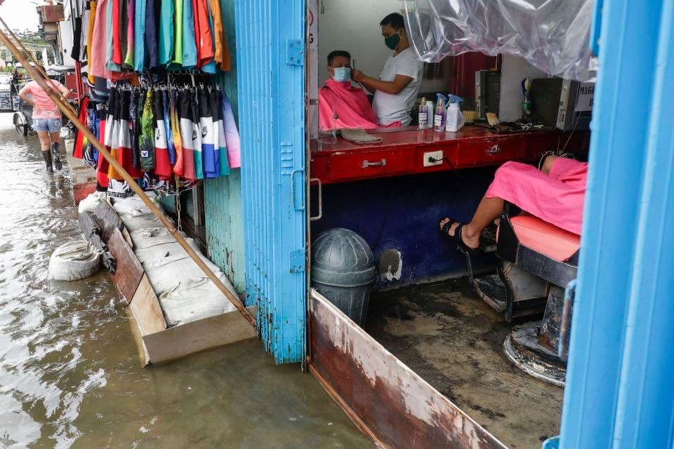 Một người đàn ông trong tiệm cắt tóc bị ngập bên ngoài ở tỉnh Pampanga, phía bắc Philippines, hôm 26/10.