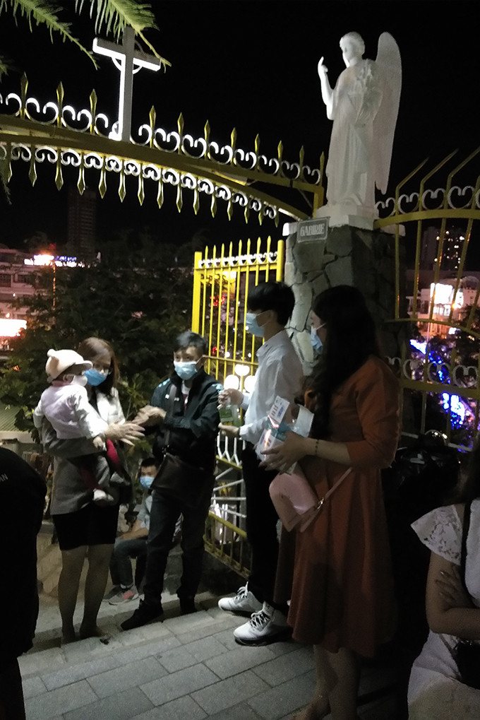 People are given masks and wash their hands with hand sanitizer before entering Nha Trang Cathedral