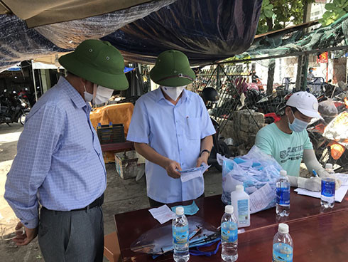 Ông Nguyễn Tấn Tuân (giữa) kiểm tra việc ghi phiếu đi chợ tại chợ Ga xã Vĩnh Thạnh