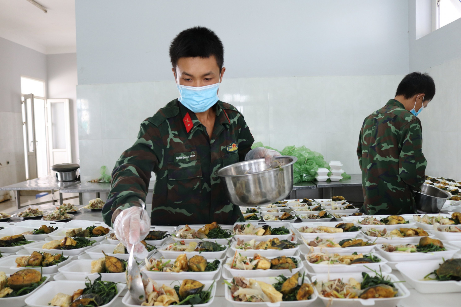 Các chiến sĩ chia cơm và thức ăn vào hộp cho người dân ở khu cách ly.
