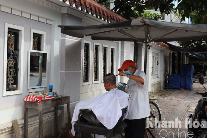 Cụ ông cắt tóc trong vùng xanh tại một khu phố ở thị xã Ninh Hòa.