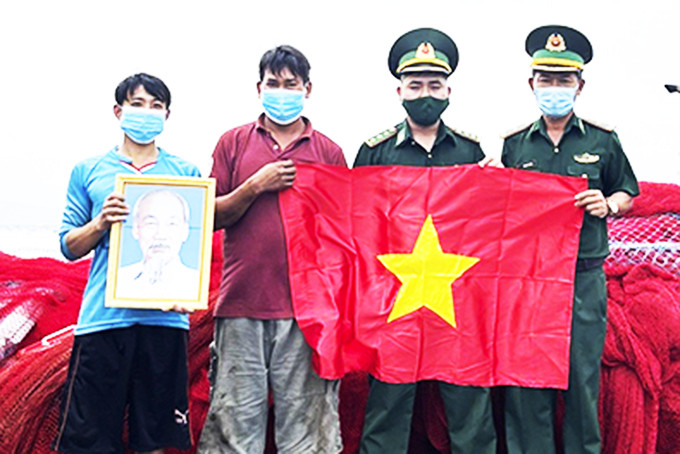 Cán bộ  Trạm Kiểm soát Biên phòng Ba Ngòi  trao cờ Tổ quốc và ảnh Bác Hồ cho ngư dân.