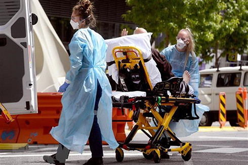 Nhân viên y tế chuyển bệnh nhân Covid-19 tới bệnh viện tại Melbourne, Australia. (Ảnh: AFP/TTXVN)